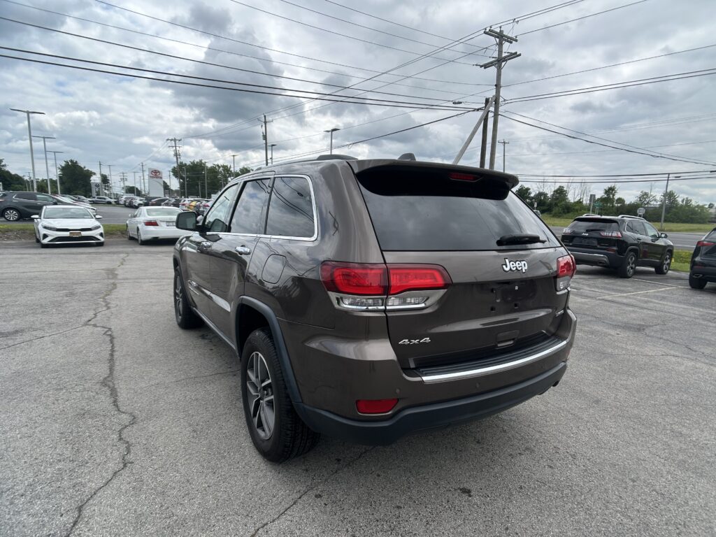 Rear view of a gray Jeep Grand Cherokee in a parking lot under a cloudy sky with power lines overhead