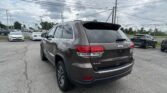 Rear view of a gray Jeep Grand Cherokee in a parking lot under a cloudy sky with power lines overhead