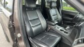 Inside a vehicle with black leather front seats and a center console with cup holders visible between them, viewed from the open driver's side door.