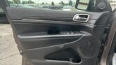 Driver-side car door interior with chrome handle, window controls, and built-in speaker; parking lot visible outside.