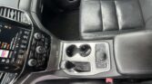 Center console view of a black leather car interior with cupholders, climate controls, and infotainment screen on the left side side of the image.