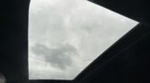 Interior of a car with an open panoramic sunroof, showing a cloudy grey sky above