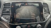 Car's dashboard screen showing rearview camera display with 'Check Entire Surroundings' warning over a parking lot scene