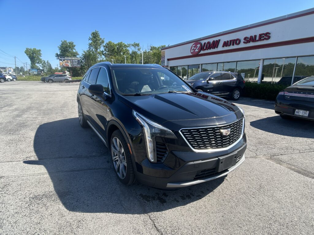Front view of a dark Cadillac SUV parked in a lot in front of EZ Auto Sales on a sunny day.