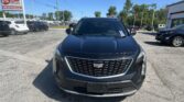 Front view of a dark blue Cadillac SUV in a car dealership lot with other vehicles and an EZ Loan sign in the background.