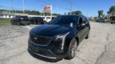 Black Cadillac SUV in the foreground at a car dealership lot with an EZ Loan Auto Sales sign and other vehicles in the background under a clear blue sky.