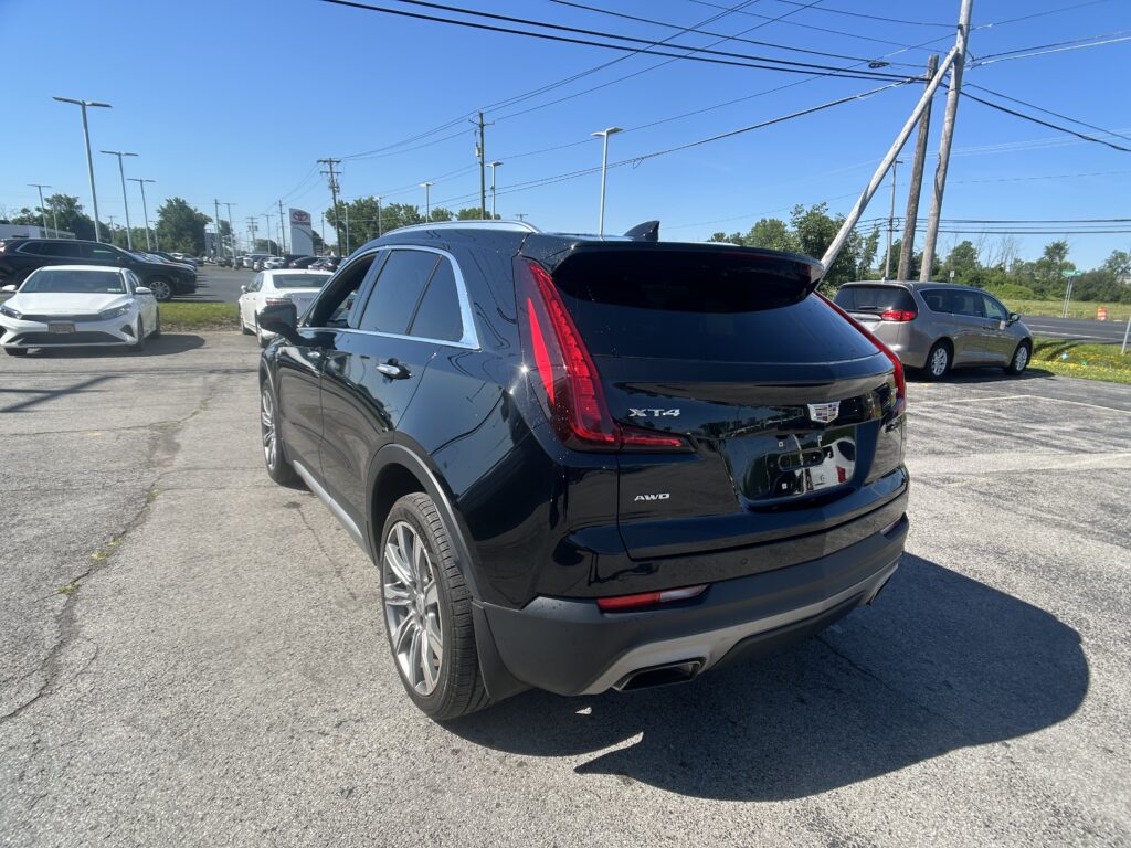 Rear view of a shiny black Cadillac XT4 SUV in a car dealership lot with other vehicles and a clear blue sky above.