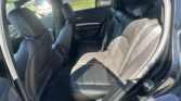 Interior view of a dark leather backseat area in a car, showing two rows of seats and seat belts ready for passengers.