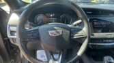 Interior view from the driver's seat showing a Cadillac steering wheel, instrument cluster, and the touchscreen infotainment display in a parked car.