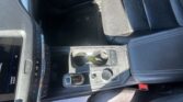 Car interior focusing on the center console: gear shifter, climate control buttons, and a touchscreen display on the left.