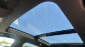 View upward through an open panoramic sunroof at a clear blue sky, with raindrops on the glass and car interior around it.