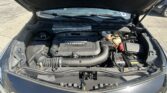 Open car hood reveals the engine bay with a prominent turbo engine cover in the center and various hoses and reservoirs visible, including a coolant bottle on the right.
