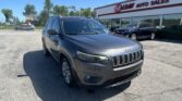 Grey Jeep SUV in foreground at a car lot with 'EZ Loan Auto Sales' building in background and clear blue sky