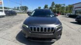 Front view of a dark gray Jeep SUV parked in a sunny car dealership lot with other vehicles nearby.