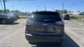 Rear view of a gray Jeep Latitude SUV in a crowded parking lot on a sunny day, with power lines and street lamps in the background.