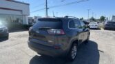 Jeep SUV in a dealership lot with other cars and a white building on the left, under a clear blue sky.