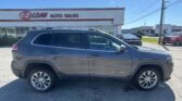 Gray Jeep Cherokee SUV in a dealership parking lot with E-Z Loan Auto Sales sign in the background on a sunny day