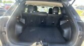 Open SUV trunk showing large cargo space with folded rear seats, black interior, and parked cars visible outside.
