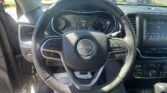 Driver's view of the Jeep interior focusing on the steering wheel and dashboard, with a dealership parking lot visible outside the windshield.