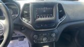 Driver's-seat view of a car interior: center touchscreen radio on the dashboard showing FM stations (107.9) with surrounding vents and climate controls nearby.
