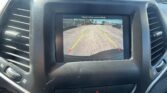 In-dashboard rearview camera display showing parking-lot scene with colored guide lines (green/yellow) and a red stop line; text reads 'Check entire surroundings'.