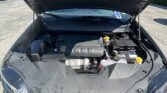 Open-hood view of a car engine bay in a parking lot, with various engine components visible under sunlight