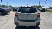 Rear view of a gray Subaru Crosstrek in a busy car lot, other cars parked nearby under a clear blue sky.