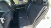 Rear passenger seat area of a car with black fabric seats and orange stitching; parking lot visible through the windows.