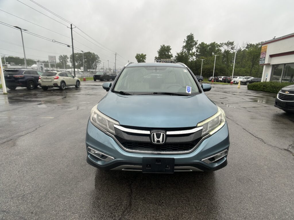 Front view of a blue Honda SUV in a car dealership lot on a rainy day, with wet pavement and other cars in the background.