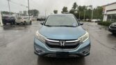 Front view of a blue Honda SUV in a car dealership lot on a rainy day, with wet pavement and other cars in the background.