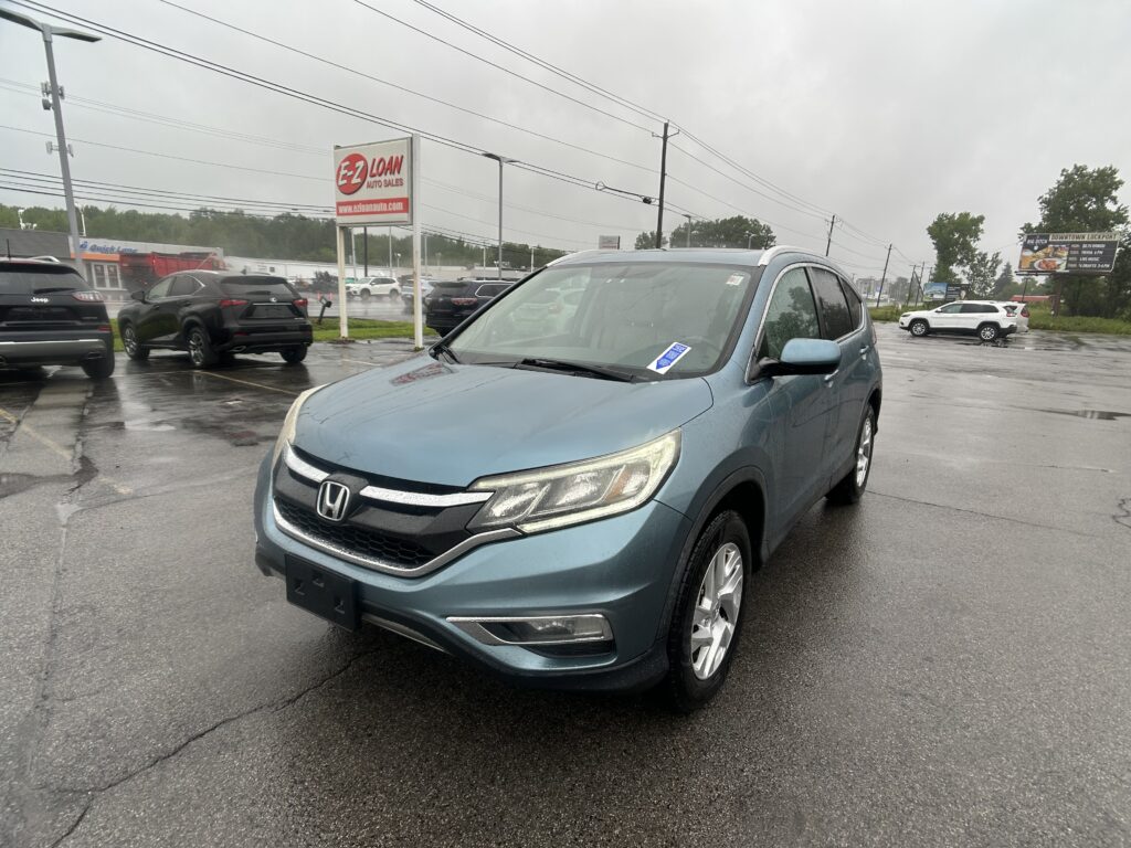 Blue Honda SUV in the foreground at a rainy car dealership lot, with puddled pavement and other parked cars behind it.
