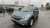 Blue Honda SUV in the foreground at a rainy car dealership lot, with puddled pavement and other parked cars behind it.