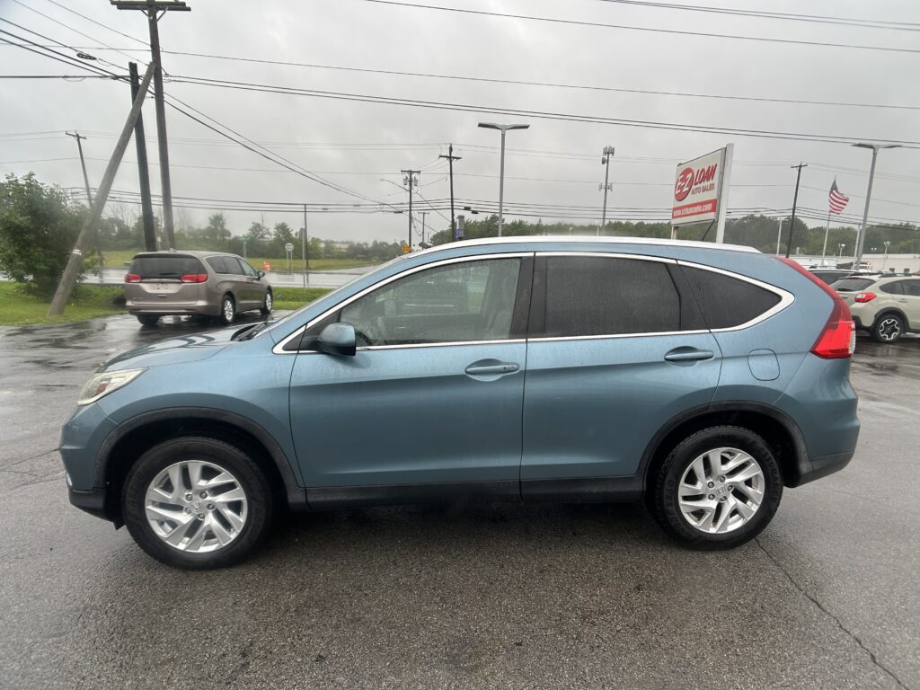 Close-up side view of a blue SUV parked in a wet parking lot, with overcast skies and power lines in the background.