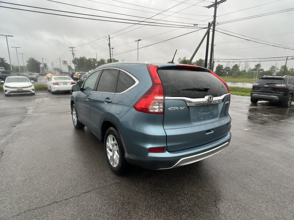 Blue Honda CR-V parked in a rain-soaked lot with other cars and overhead power lines visible in the distance.