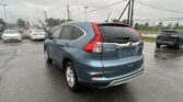 Blue Honda CR-V parked in a rain-soaked lot with other cars and overhead power lines visible in the distance.