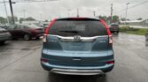 Rear view of a blue Honda CR-V AWD parked in a wet parking lot under a gray, cloudy sky with other cars around.