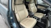 Interior of a car with tan leather front seats, center console, and an open door on a rainy day outside.