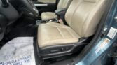 Interior of a car showing the driver and front passenger beige leather seats, black center console, and steering wheel on the left side, with a window and door panel visible on the right and rain on the glass outside.