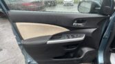 Interior of a car door panel with beige and black upholstery; rain-soaked window reveals a parking lot outside.