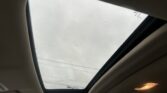 Interior view from a car cabin looking up at a panoramic sunroof, cloudy sky visible through the glass with water droplets on the pane.