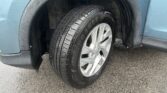 Close-up of a vehicle's front wheel with a treaded tire mounted on a silver alloy rim, in a wet asphalt lot.