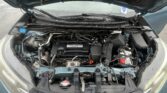 Open car hood exposing engine bay with battery, hoses, and wiring visible on a blue vehicle.