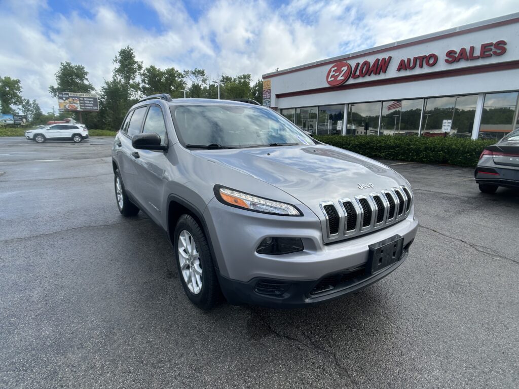 Silver Jeep SUV in the foreground of EZ Auto Sales storefront, parking lot and blue-sky clouds behind.