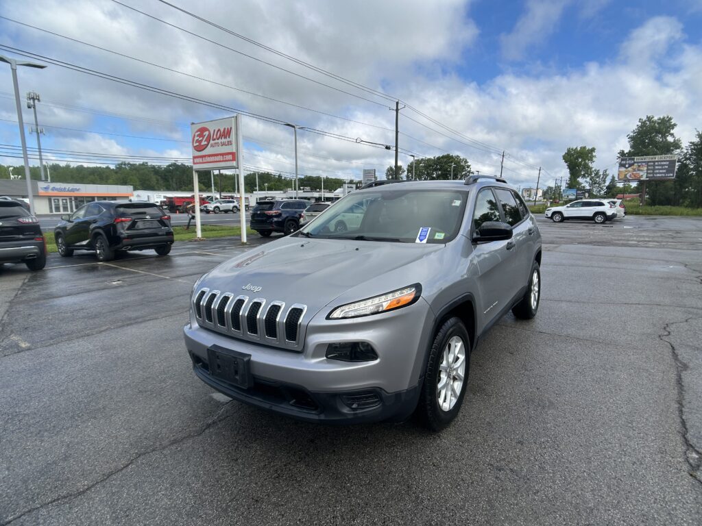 Silver Jeep SUV in a dealership lot with other cars and EZ LOAN Auto Sales sign in the background