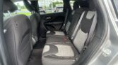 Interior of a car’s back seat showing three dark fabric seats with shoulder belts and visible door panel on the right side.