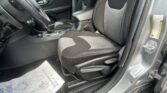 Dark cloth car interior showing front driver and passenger seats with center console and steering wheel from the driver’s open door side.