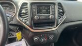 Center dash of a pickup showing the built‑in radio screen and control knobs, with climate dials below and a paper flyer on the floor to the left reading We Take Pride in Your Vehicle.