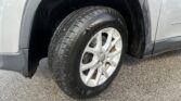 Close-up of a car tire and silver alloy wheel inside the front wheel well of a gray SUV.