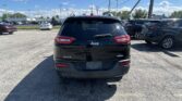 Rear view of a black Jeep SUV in a crowded dealership lot with other cars and power lines overhead under a blue sky with clouds