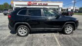 Black Jeep Cherokee SUV in the foreground with EZ Loan Auto Sales storefront and a bright blue sky in the background.
